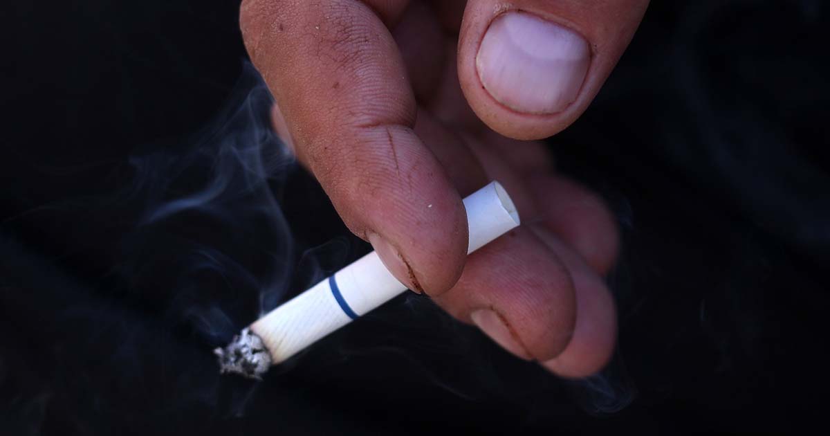 Fumante segurando cigarro entre os dedos
