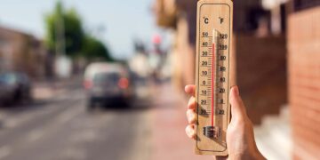 Clima quente. Termômetro na mão em frente a uma cena urbana durante a onda de calor | Foto: Shutterstock