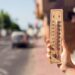Clima quente. Termômetro na mão em frente a uma cena urbana durante a onda de calor | Foto: Shutterstock