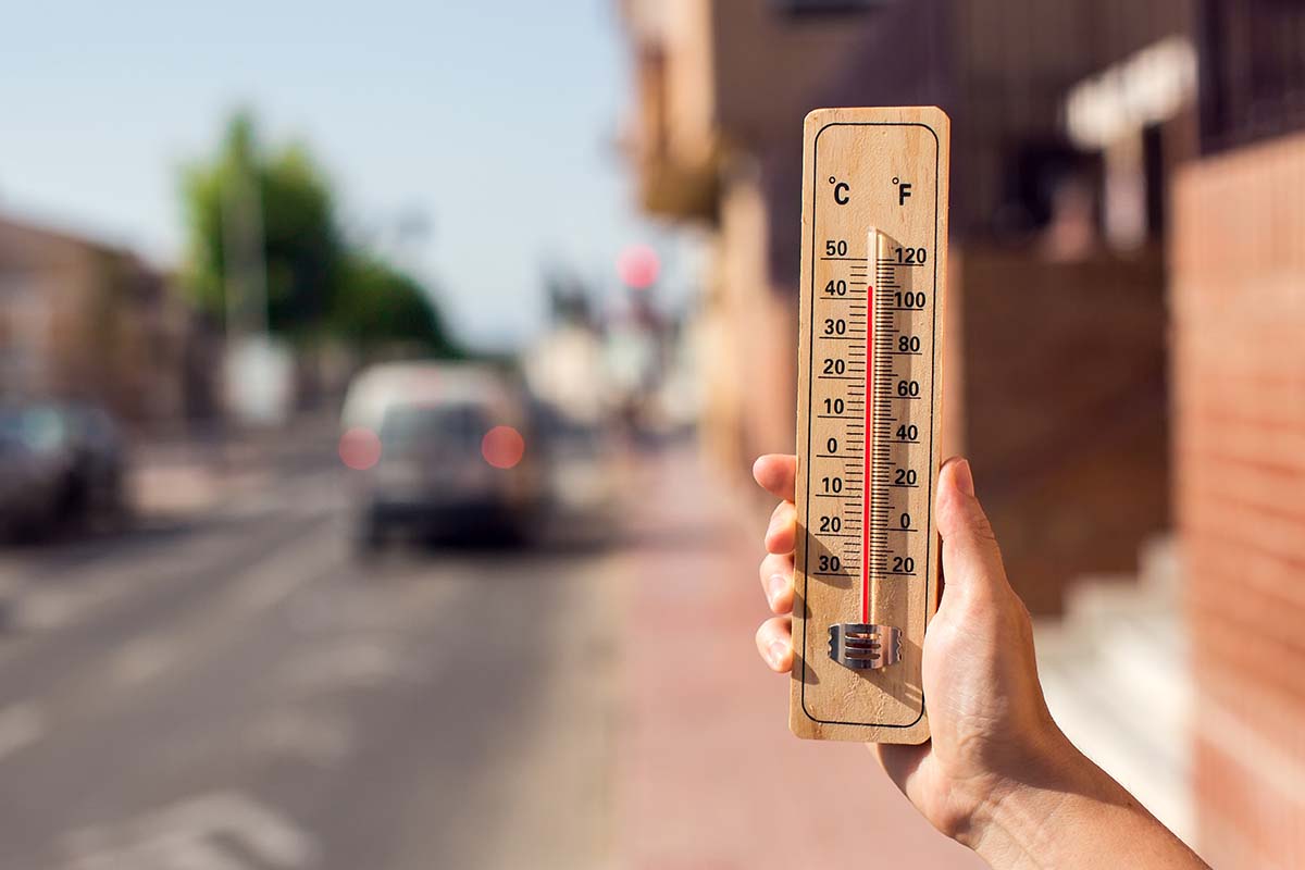 Clima quente. Termômetro na mão em frente a uma cena urbana durante a onda de calor | Foto: Shutterstock