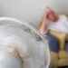 Mulher idosa em um sofá sofrendo de calor excessivo durante uma onda de calor e sendo resfriada por um ventilador elétrico oscilante em primeiro plano | Foto: Shutterstock